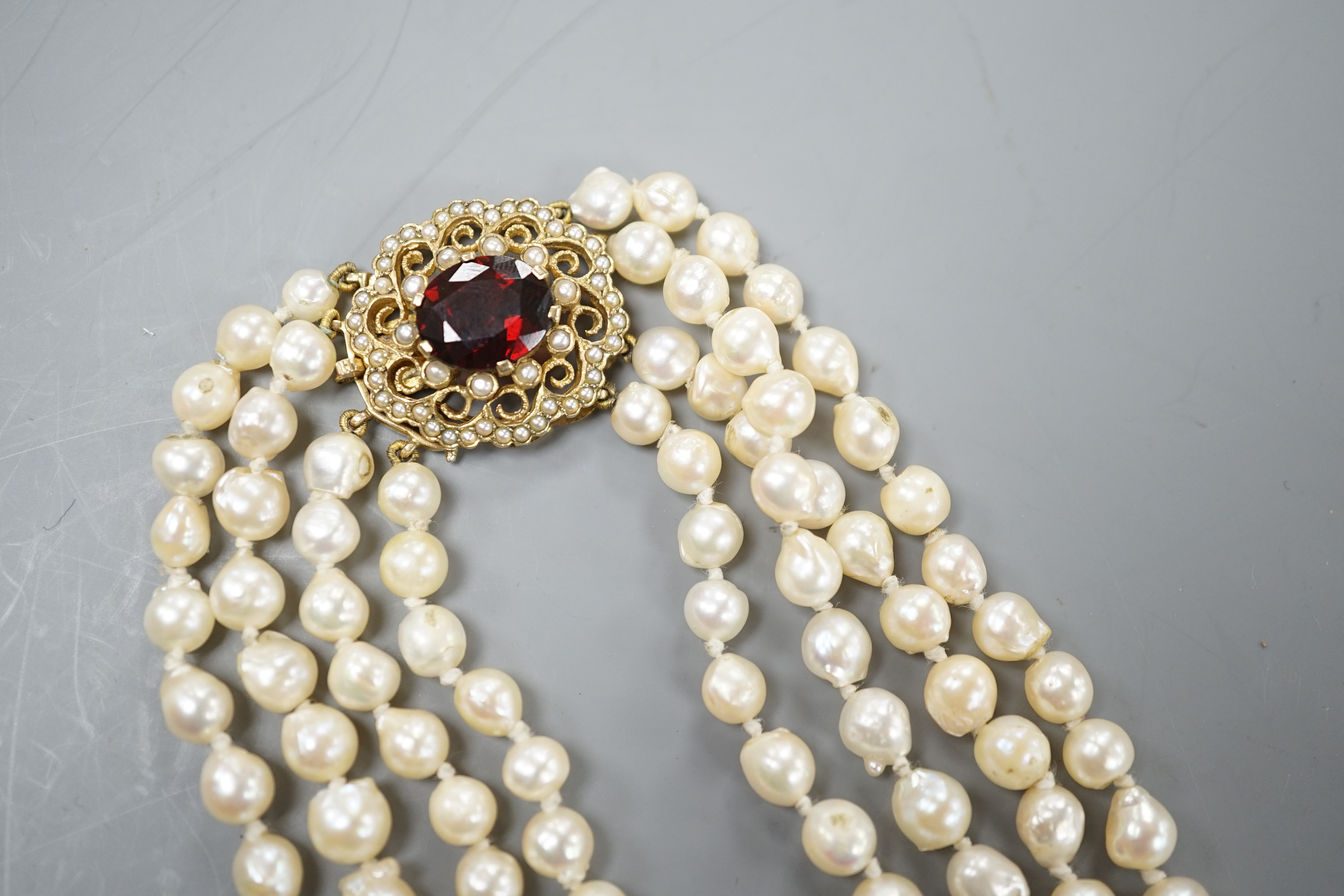 A 1960's triple strand cultured pearl necklace, with garnet and seed pearl set 9ct gold clasp, 48cm.